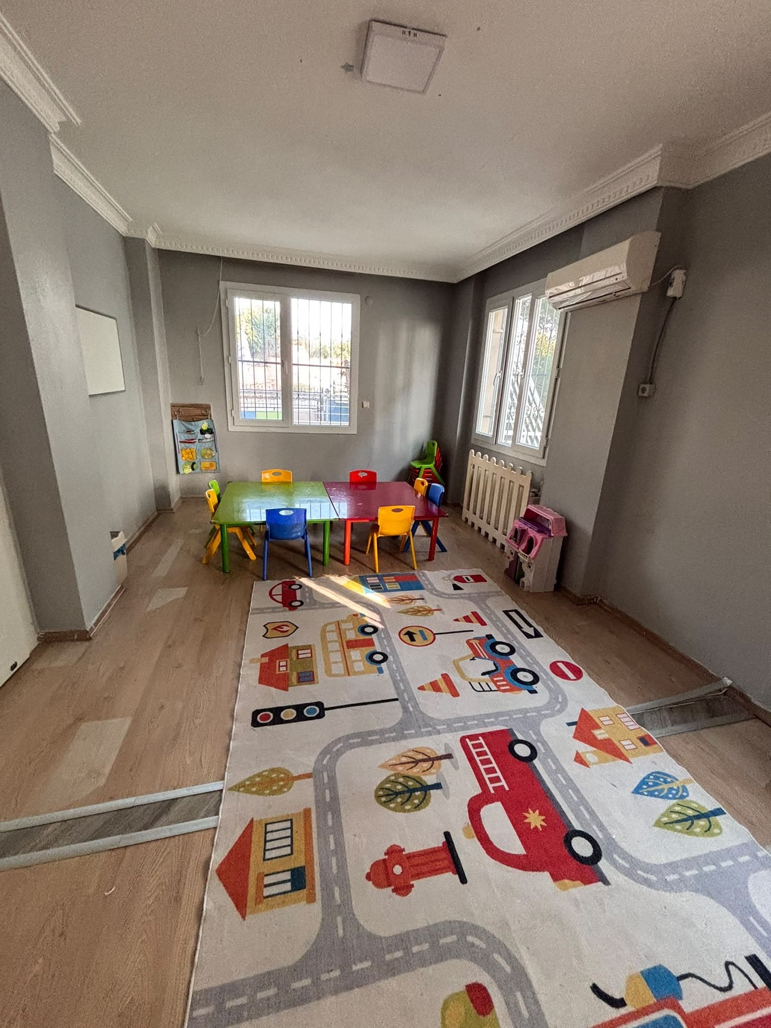 Oyun halısı ve çalışma masası bulunan aydınlık sınıf